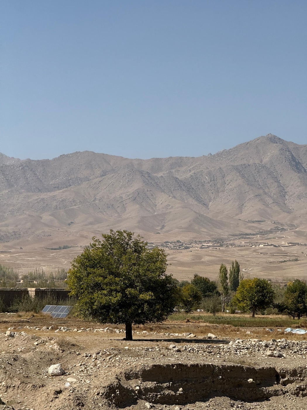 A green valley and village beneath dry mountains